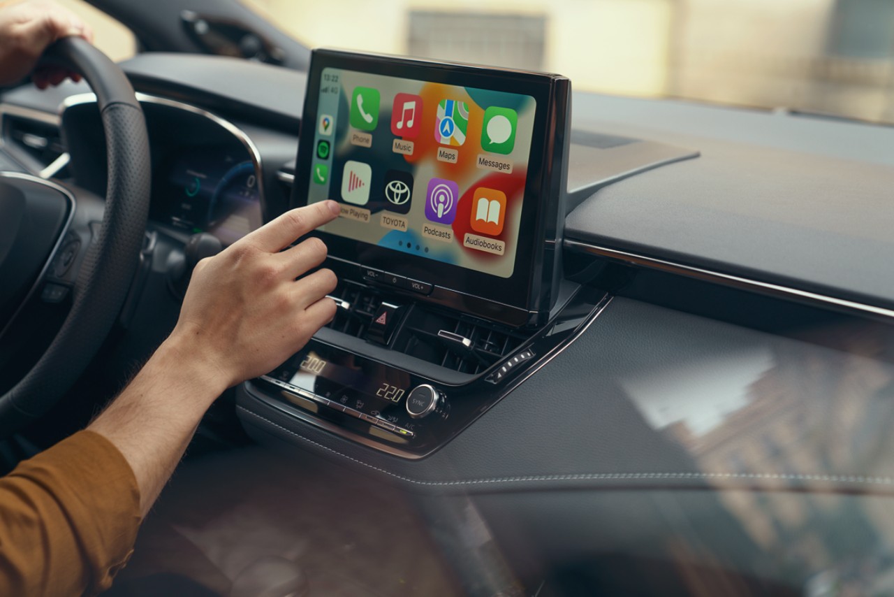 Eine Person in einem Toyota bedient den Multimedia-Bildschirm des Fahrzeugs. Er zeigt die Home-Seite von Apple CarPlay.